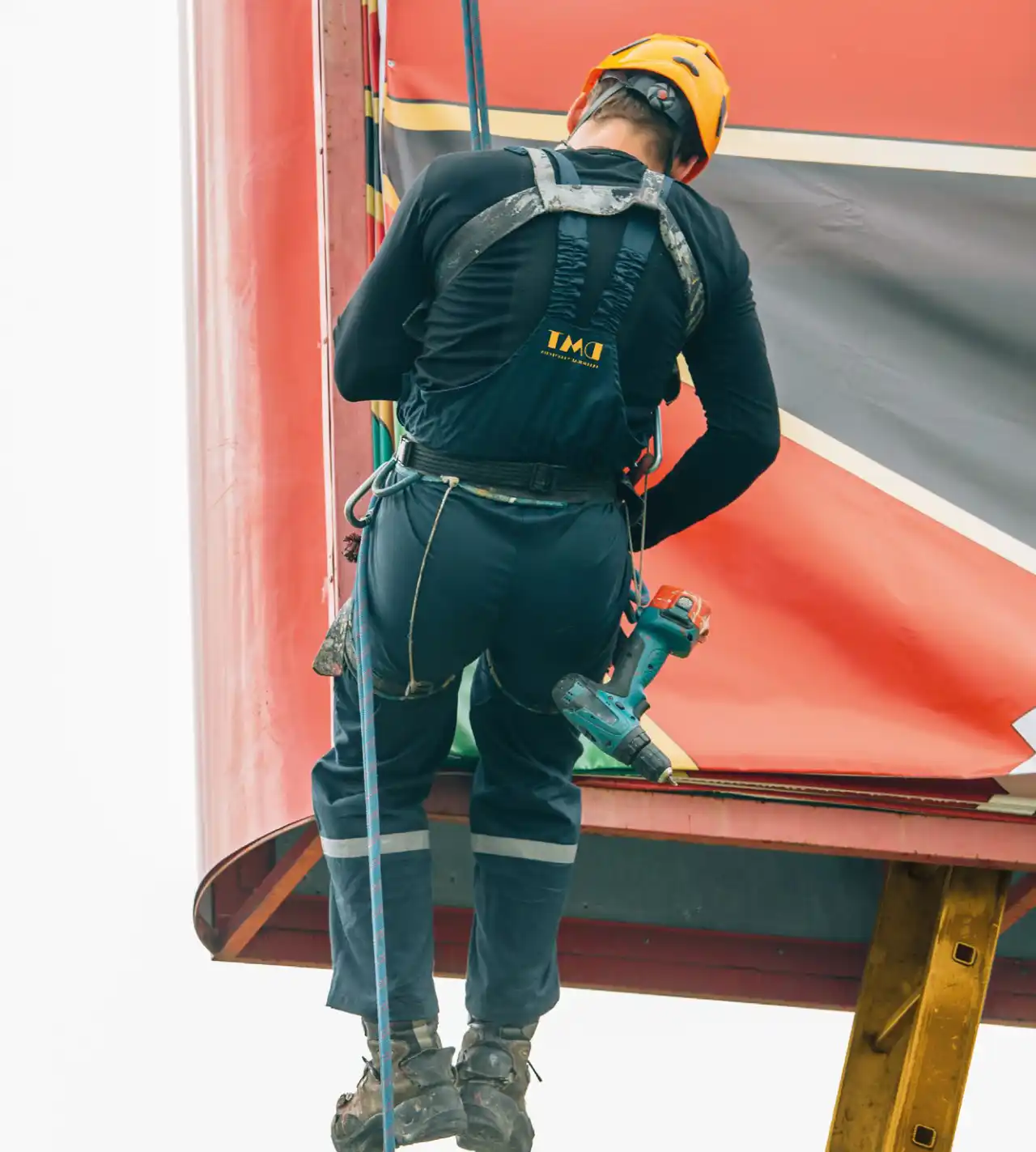 Técnico de DMT con arnés de seguridad instalando lona publicitaria en estructura de espectacular